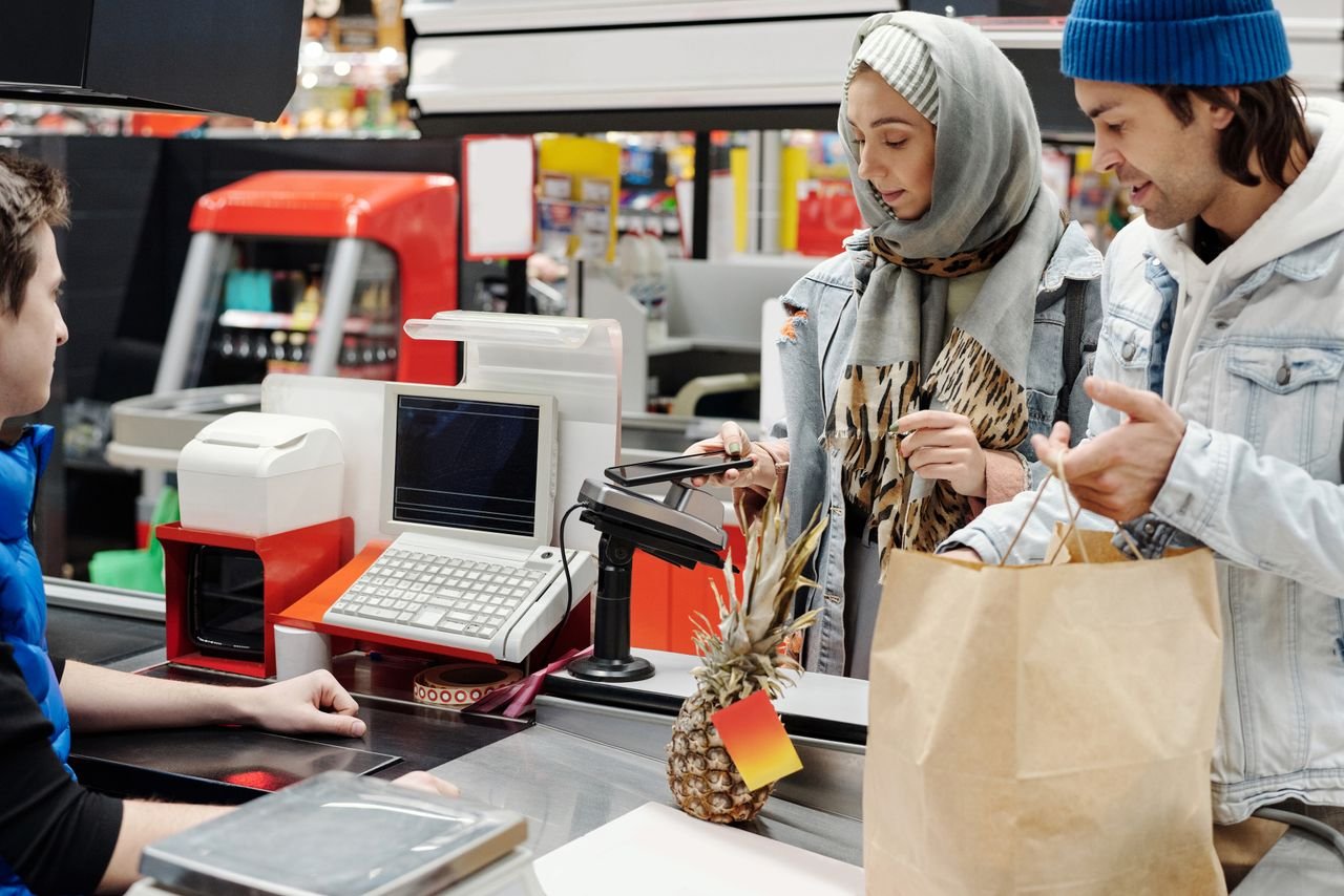 Crafting Captivating Headlines: Your awesome post title goes here A couple in a supermarket checkout using mobile payment with a cashier. Modern retail technology.