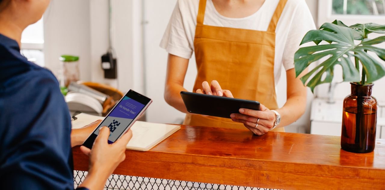 services-04 Crop anonymous female employee with application on cellphone screen interacting with partner using tablet at counter in cafeteria
