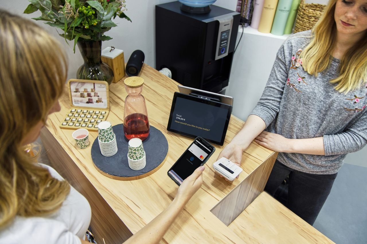 Mastering the First Impression: Your intriguing post title goes here A woman makes a contactless payment at a stylish Berlin café, emphasizing technology and modern retail.