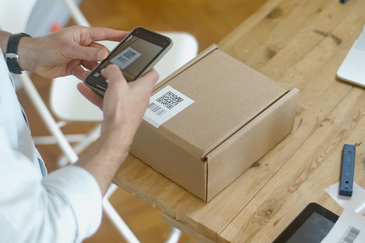 services-02 A person uses a smartphone to scan a QR code on a package in an online store setting.