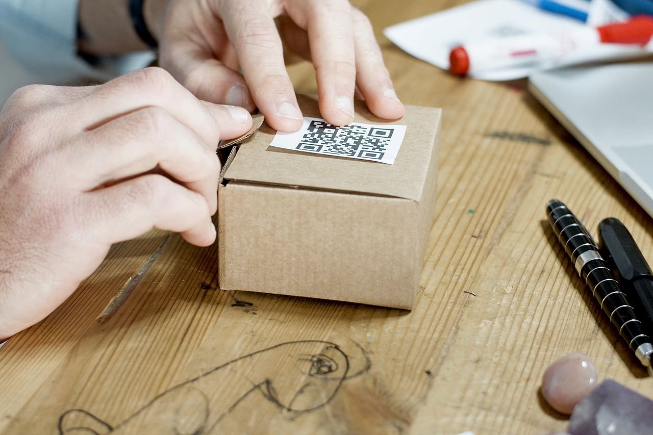 services-01 Close-up of hands packing a box with a QR code, symbolizing online business services.