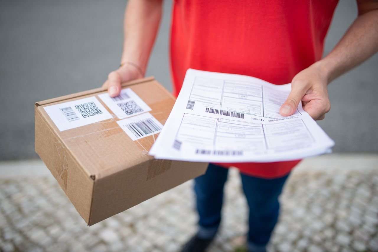 The Art of Drawing Readers In: Your attractive post title goes here Close-up of person in red shirt holding a brown package and delivery documents outside.