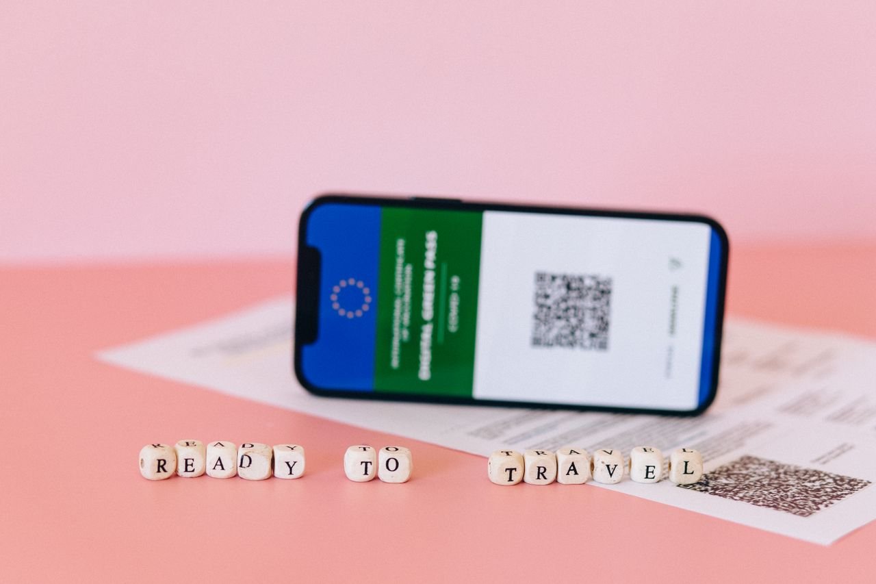 about-us-02 Smartphone displaying digital green pass on a pink surface with travel beads.