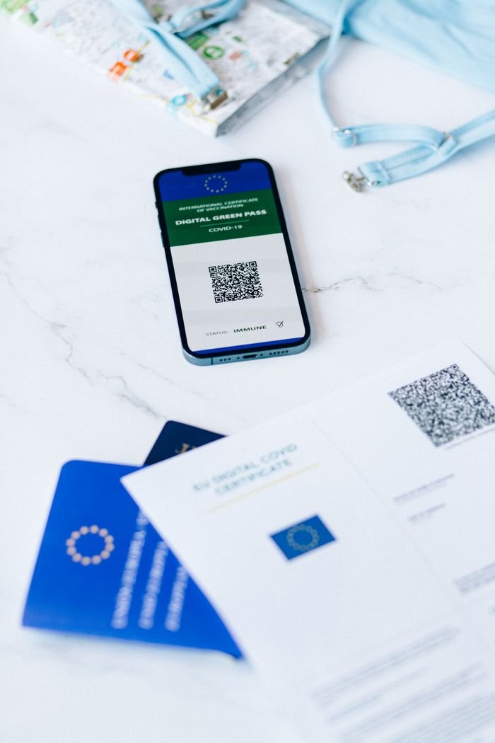 about-us-02 A smartphone displaying a digital vaccine passport alongside Covid-19 documents on a table.